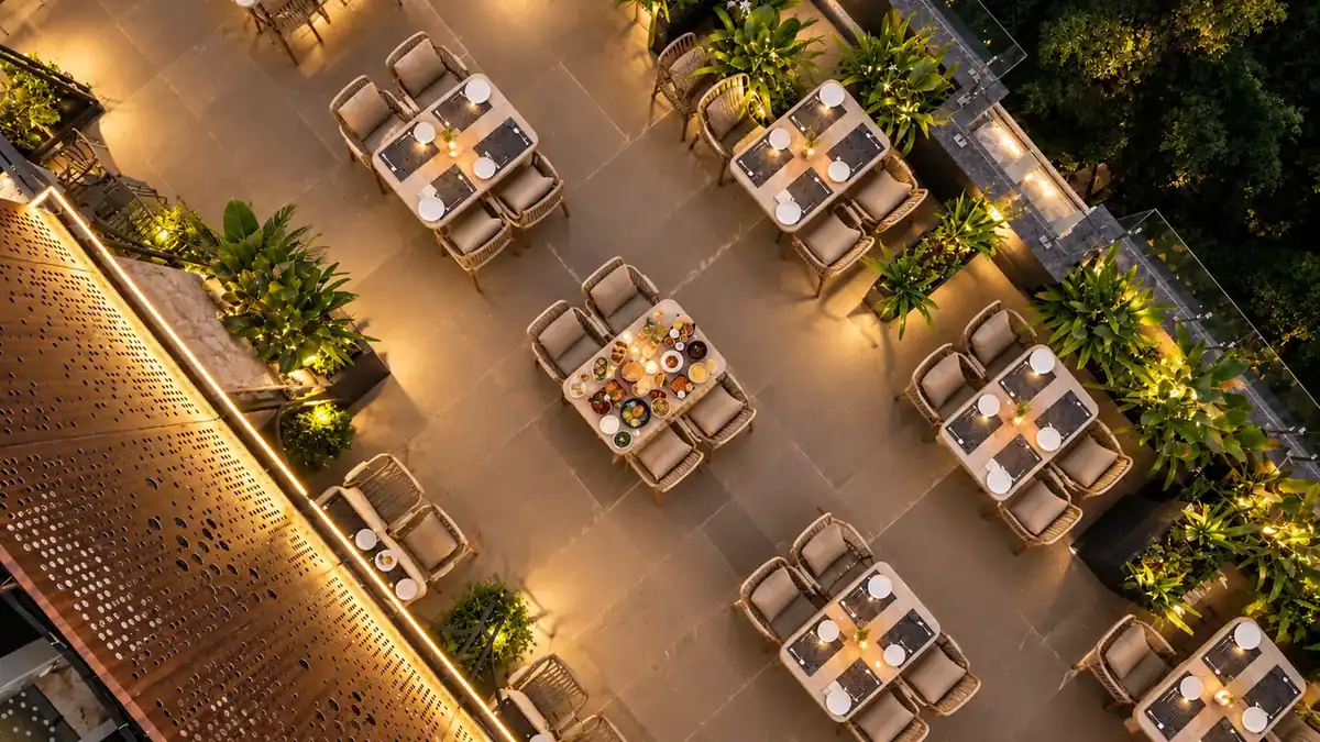 Aerial view of open-air rooftop terrace dining tables surrounded by lush foliage and fairy lights